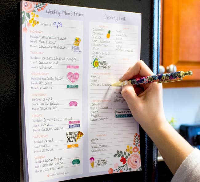 Person writes on a meal planner and grocery list attached to a fridge. Text highlights sturdy magnets for organizing weekly meals and grocery items
