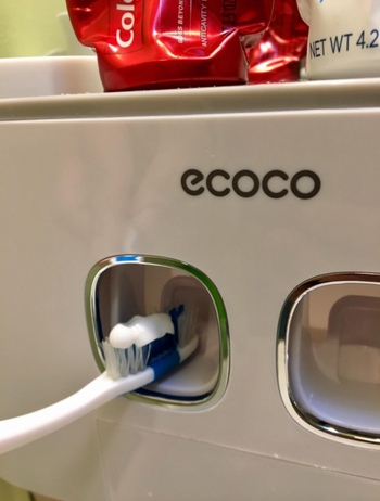 close up showing a toothbrush getting paste from the dispenser 