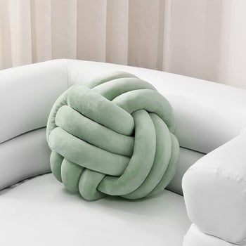 A sage green pillow in the shape of a complex knot 