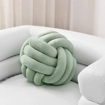 A sage green pillow in the shape of a complex knot 