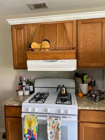 A reviewer's Kitchen with wooden cabinets, a stove, and various items like a tea kettle and fruits before the paint 