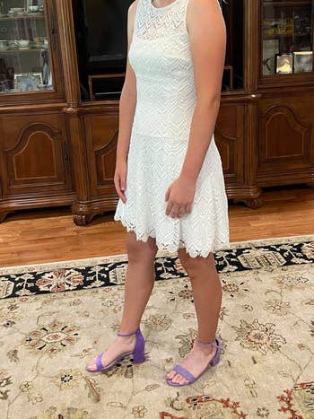 Person wearing a sleeveless lace formal and purple strappy sandals stands connected a patterned rug successful beforehand of woody cabinets