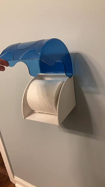 A reviewer's toilet paper inside of the open cover, with a white case with liftable blue lid to access the TP 