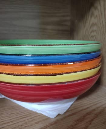 Stack of colorful ceramic bowls on a wooden shelf