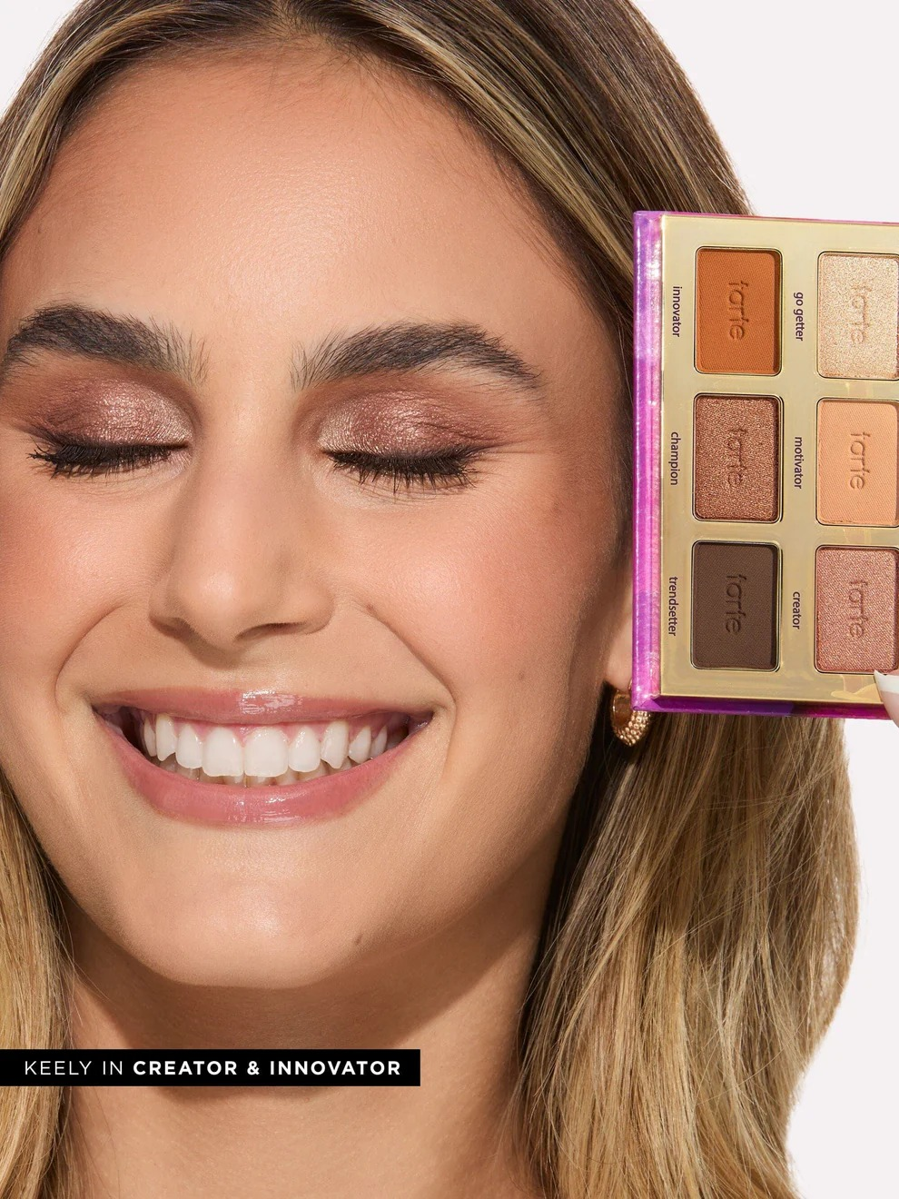 Person smiling with eyes closed, holding a constitution  palette adjacent   face, showing eyeshadow shades