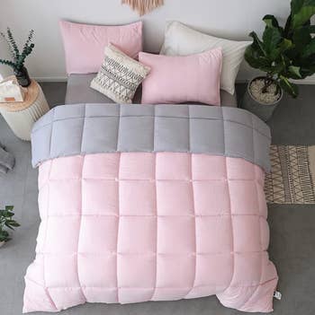 Pink and gray reversible square stitched comforter with pink pillowcases against a white wall
