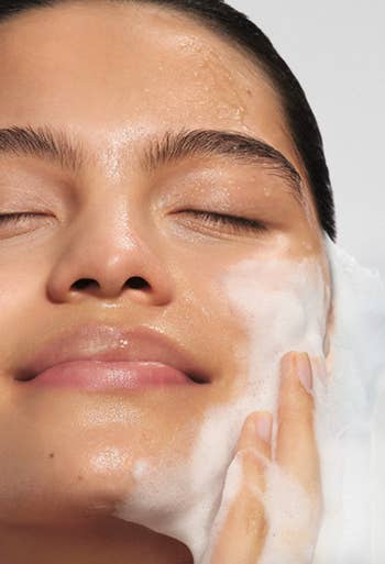 A idiosyncratic   with closed eyes smiles portion    lathering their look   with foamy cleanser, illustrating a skincare routine