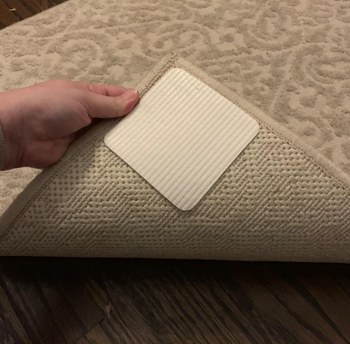 Reviewer lifting rug corner to show white square rug gripper on the bottom 