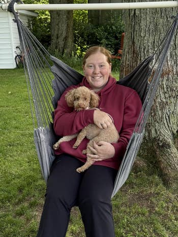 Person sitting connected  a hammock, smiling and holding a tiny  canine   