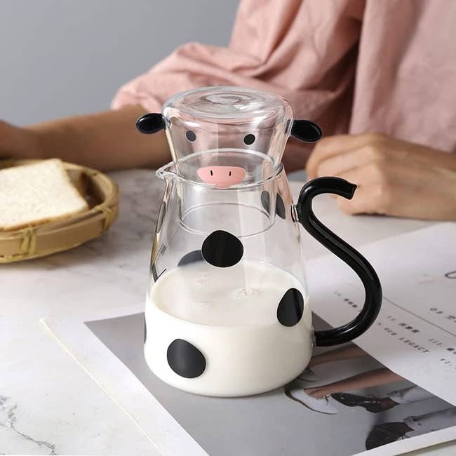 clear pitcher with black spots and curly black tail handle and cup with cow face that fits on top