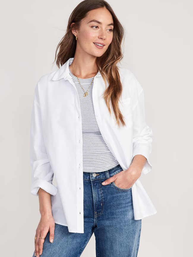 A idiosyncratic   wears a casual outfit with a striped shirt, unfastened  achromatic  button-down, and jeans, styled for a relaxed, mundane  look