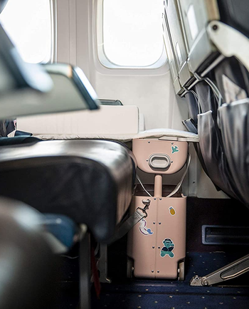 the suitcase in front of an airplane seat, with it raised up, creating a leg rest for kids to make the seat more comfortable