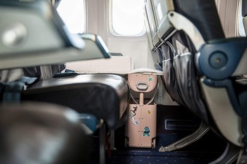 the suitcase in front of an airplane seat, with it raised up, creating a leg rest for kids to make the seat more comfortable