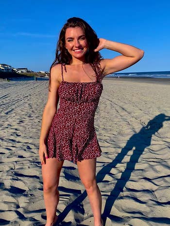 reviewer posing on the beach wearing red romper