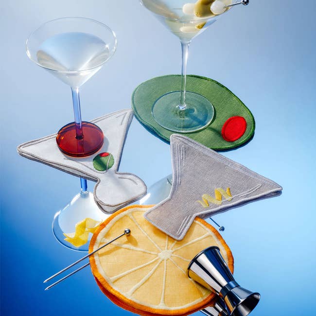 Martini glasses with cocktail-themed coasters and garnishes, accompanied by a jigger and cocktail picks, connected  a reflective surface