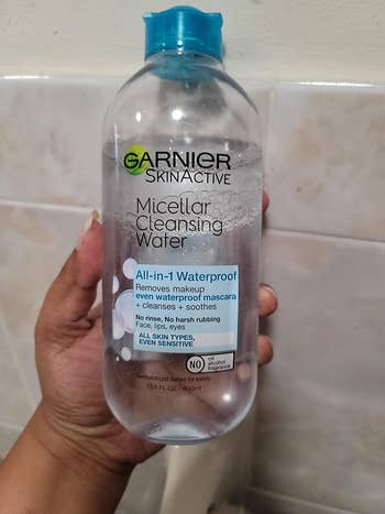reviewer photo of them holding a clear bottle of micellar water with a blue cap