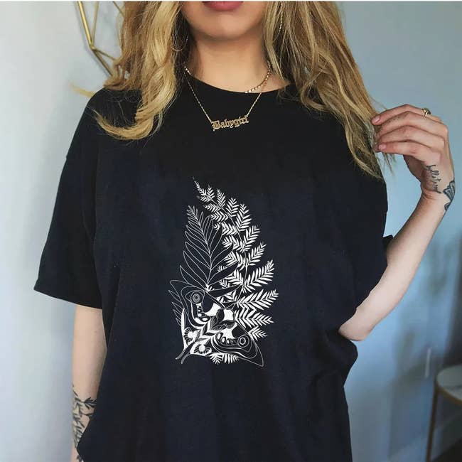 a model in an oversized black tee with a graphic of a moth over two leafy plants