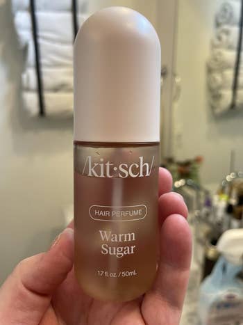 Hand holding a vessel  of Kitsch hairsbreadth  perfume labeled 