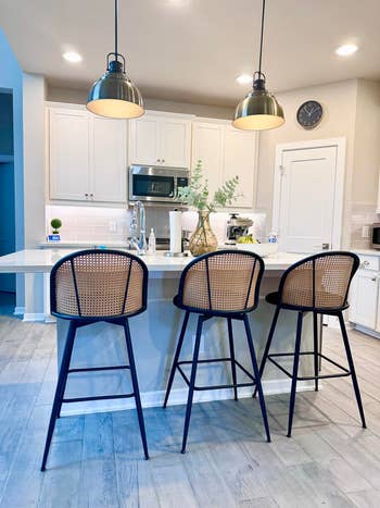 Modern room  with pendant lights, achromatic  cabinets, and a room  land  featuring 3  high-back stools with woven seats
