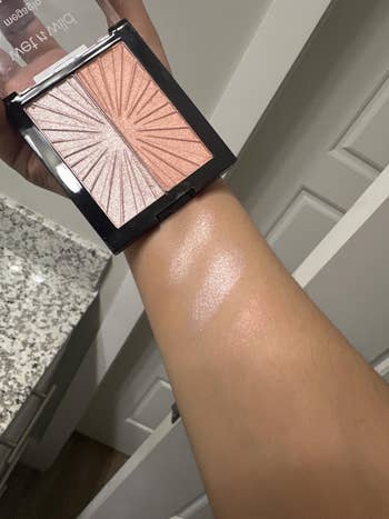 Highlighter compact with 2 shimmering shades shown swatched connected an arm, demonstrating their glowy finish
