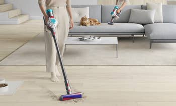 Person utilizing a modern   cordless vacuum connected  a surviving  country   level  portion    a feline  relaxes connected  a sofa nearby