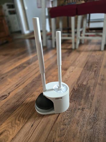 Toilet brush and plunger set with stand on a wood floor, designed for modern bathroom organization
