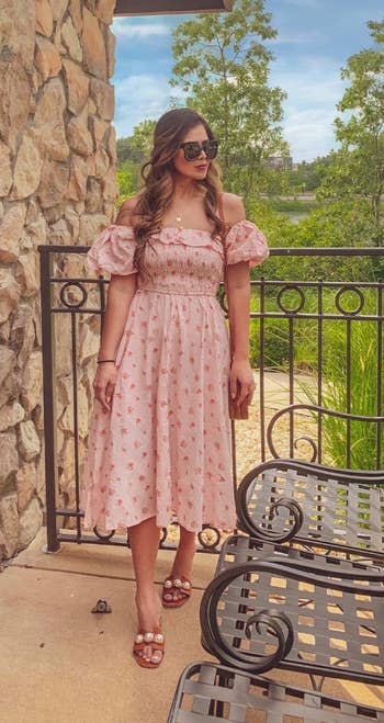 Woman in a pink floral puff-sleeve dress and sandals standing on a balcony