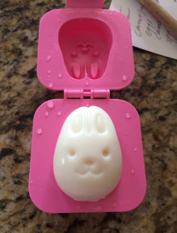 Molded hard-boiled egg resembling a bunny face, in a pink mold with lid open