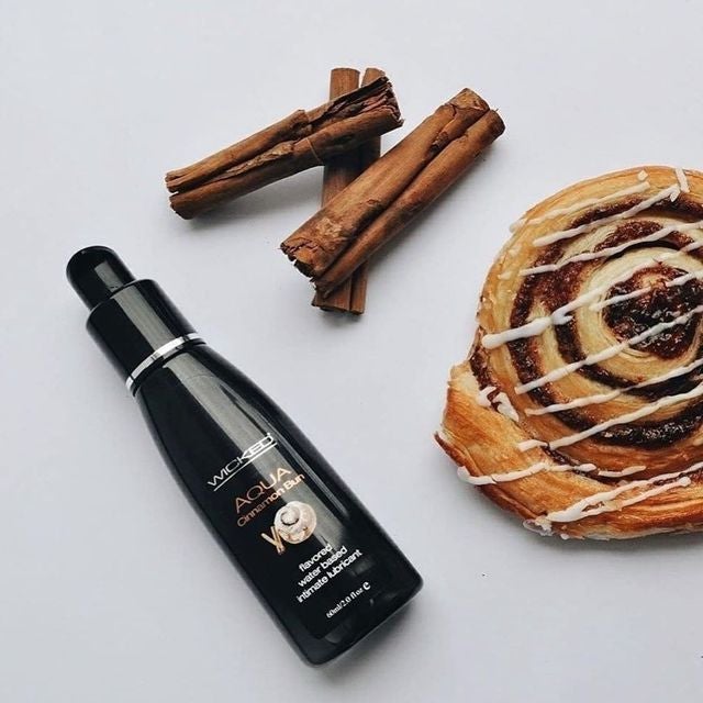 Black bottle of lubricant with cinnamon sticks and cinnamon roll