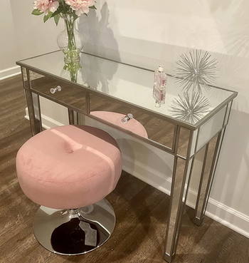 reviewer photo of the mirrored table holding a vase of flowers and some decorative items, with a pink stool in front of it