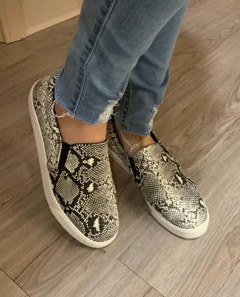 reviewer in snakeskin-print slip-on sneakers and distressed jeans