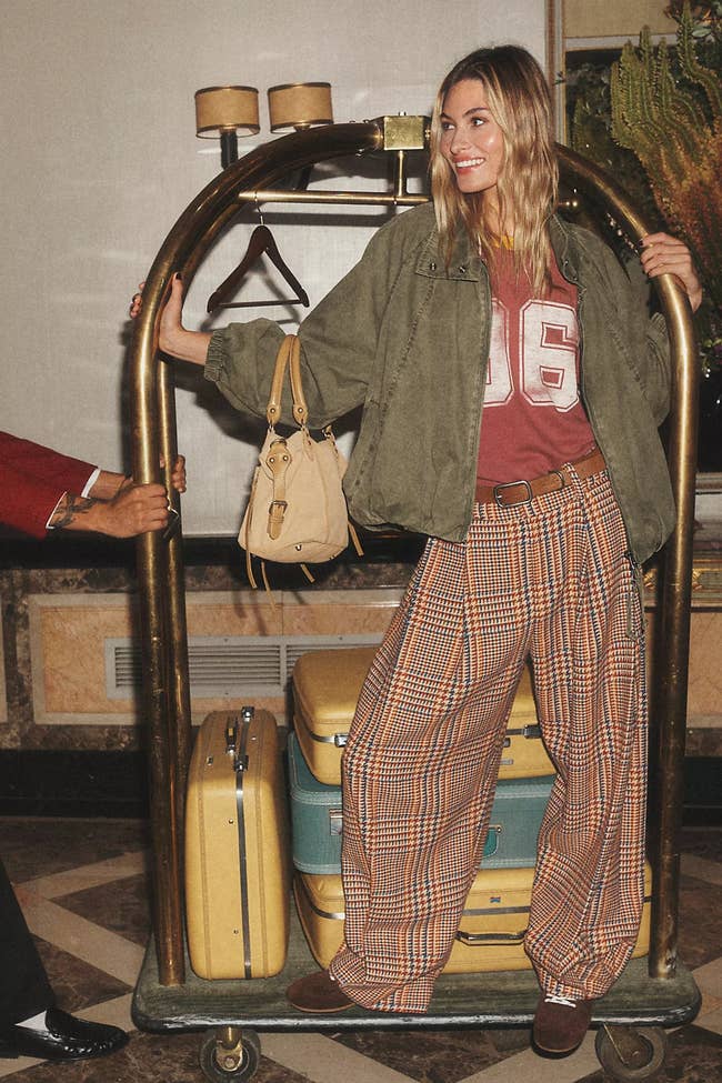 Person wearing laid-back checkered pants, a sporty top, and a casual jacket, lasting  connected  luggage cart with suitcases, successful  a travel-themed manner  shoot