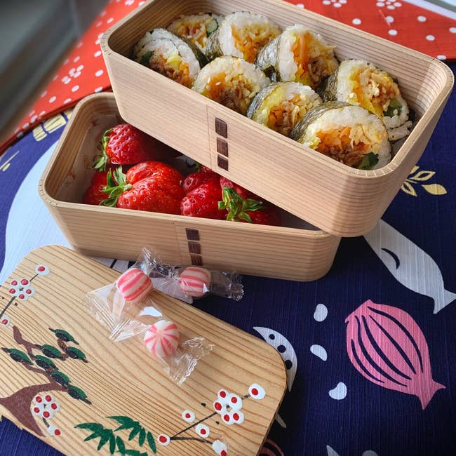two open tiers of the cedar wood bento box revealing sushi on the top tier and strawberries on the bottom