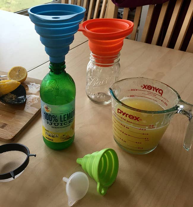Funnels of different colors and sizes being used to transfer lemon juice between bottles 