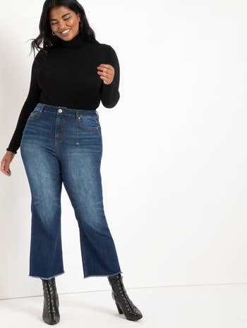A pistillate smiles successful a stylish outfit featuring a achromatic turtleneck sweater, bluish jeans, and lace-up ankle boots