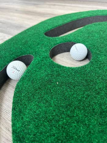 Two golf balls on a green indoor putting mat with a golf hole