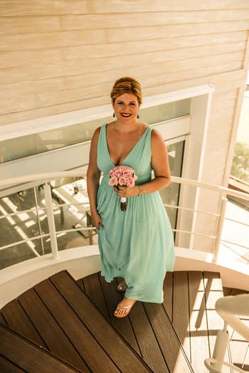 a reviewer wears the seafoam color dress while holding a pink bouquet