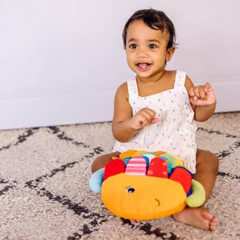 Toddler smiling with a plush toy, sitting on a carpet