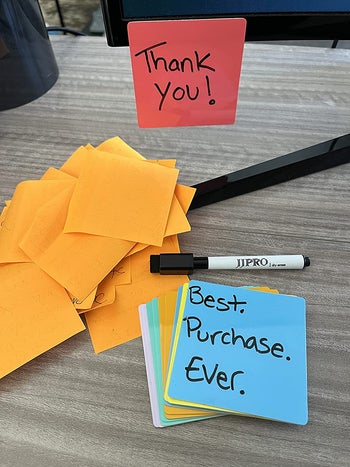 reviewer photo of the multicolored dry erase notes next to a pile of crumpled paper sticky notes, with one stuck to a mirror — they say