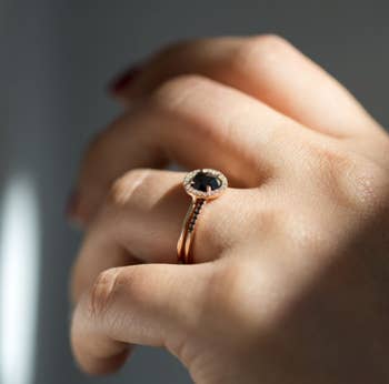 a model wearing a round engagement ring with a black diamond in the middle and a halo of diamonds around it