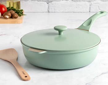 A mint-green non-stick frying pan with a lid and a wooden spatula on a kitchen counter