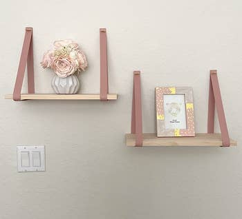 a set of two wooden shelves held up with pink leather straps