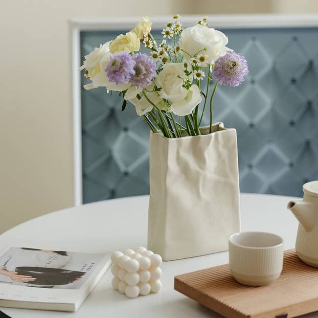 An off-white paper bag shaped vase with flowers in it 