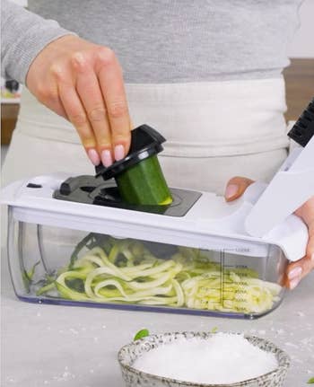 Model pressing down on top to cut a cucumber 