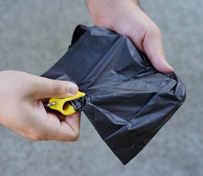 Seseorang menggunakan klip kantong plastik kuning untuk menyegel kantong sampah hitam