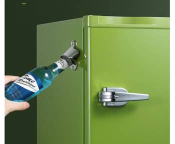 a hand opening a bottle using the bottle opener on the side of a green fridge