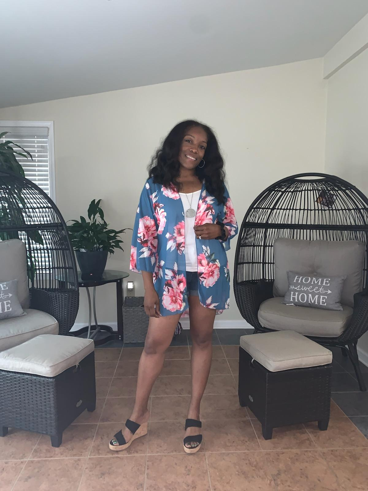 Person smiling and posing indoors, wearing a floral kimono-style outfit with level    sandals. Cozy seating country  with pillows successful  the background