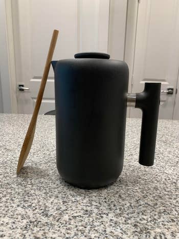 the black coffee press, with a wooden spoon next to it, showing it's just smaller than that