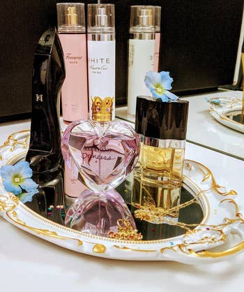 reviewer photo of perfume and other small items on a white and gold mirror being used as a tray