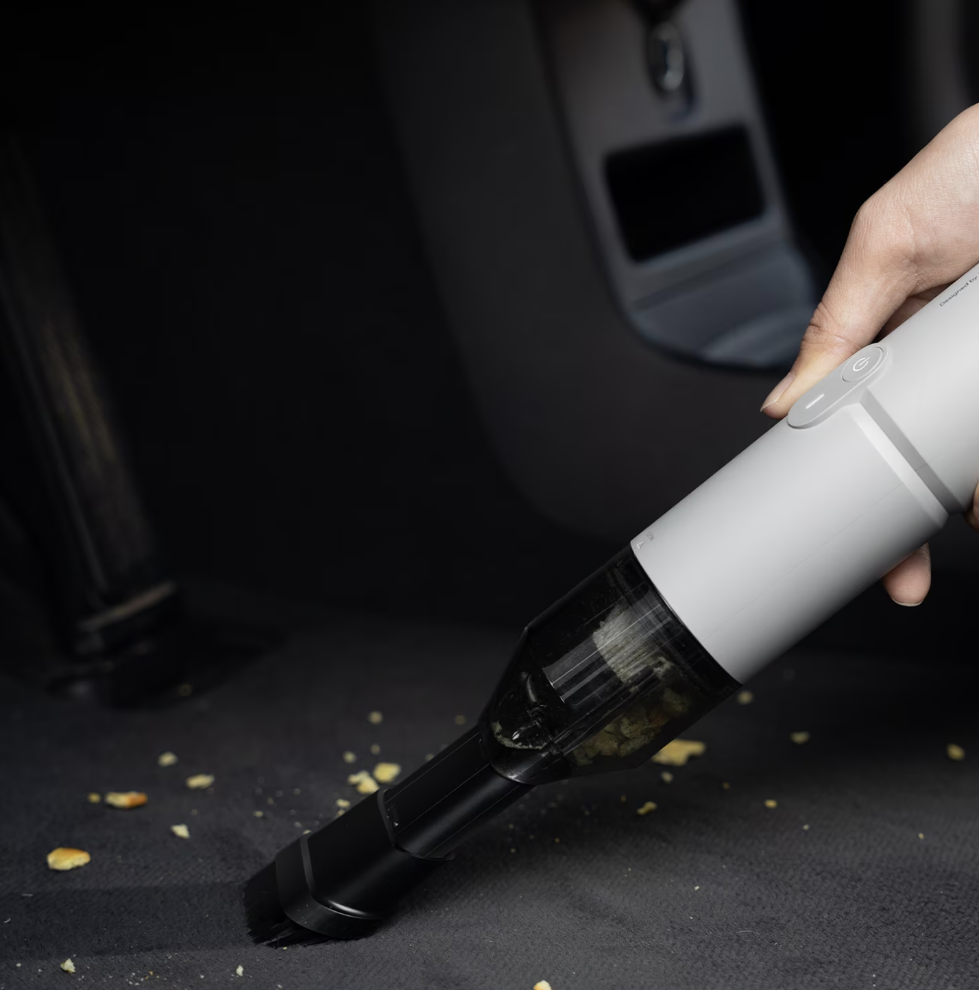 A manus  uses a portable vacuum cleaner to region   crumbs from a car   seat, showcasing cleaning ratio  and convenience for on-the-go use